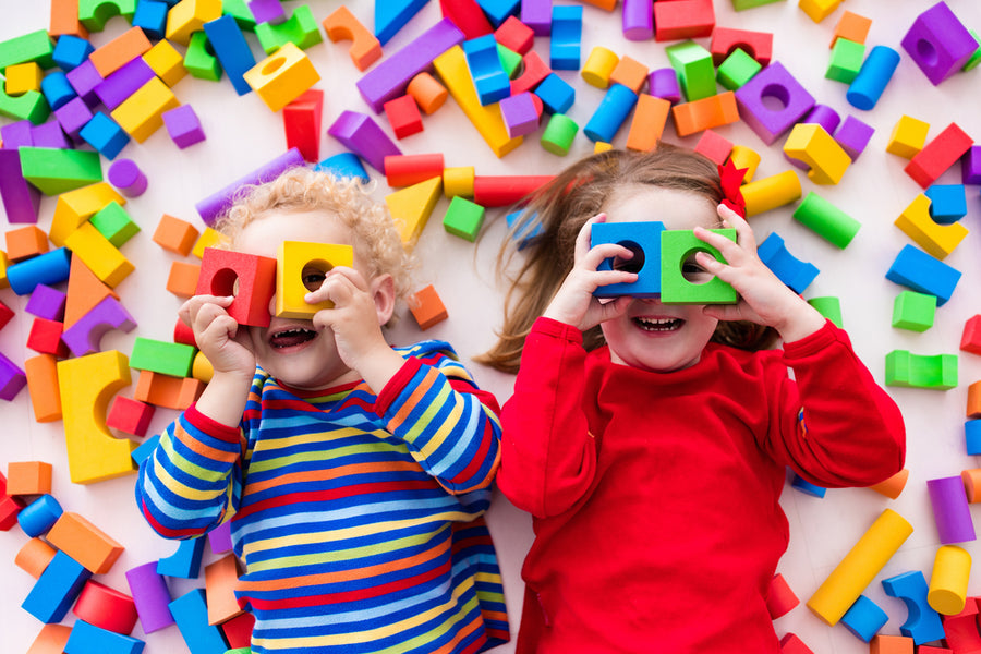 Happy 1-year-olds play with colorful plastic toy blocks.