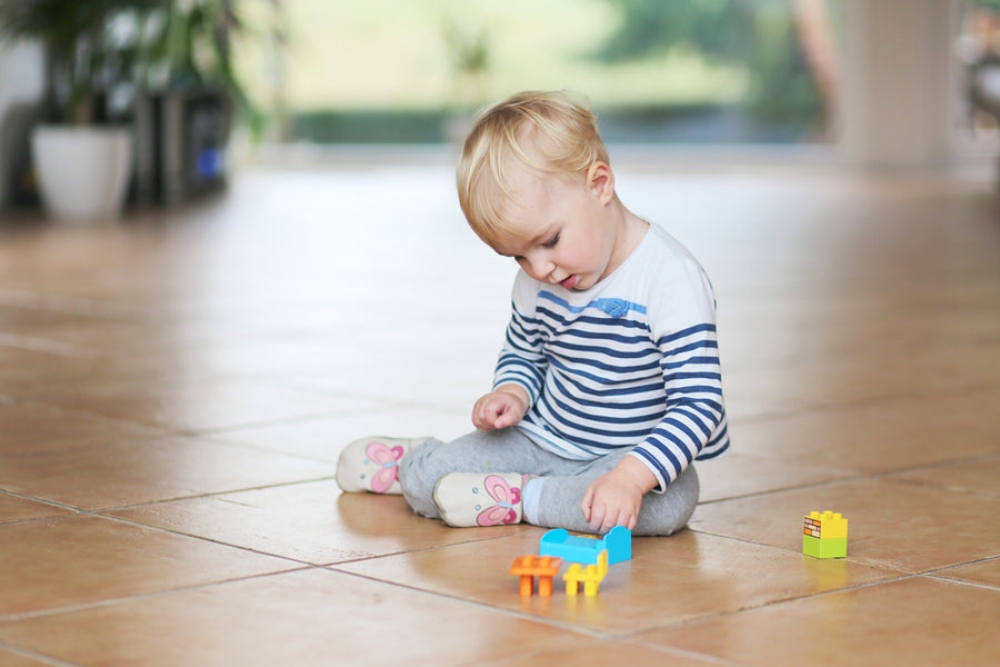 Cute little 2-year-old play with plastic bricks sitting indoors on a tiles floor